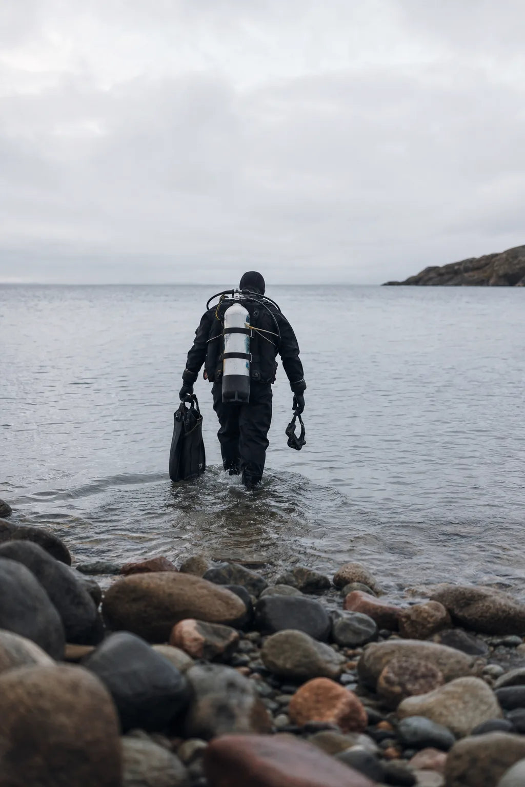 Dykker i tørdragt ved en stenet dansk strand